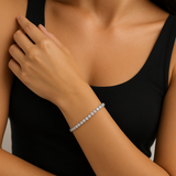Close-up of a person wearing a diamond tennis bracelet on a neutral background