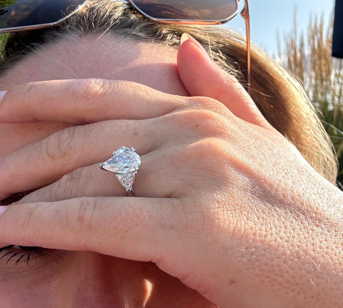 Close-up of a person wearing sunglasses with a large pear cut 3 stone diamond ring on their finger