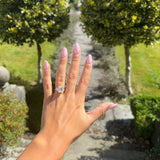 Hand with a 3 stone emerald cut diamond ring on with trees and stone path with greenery